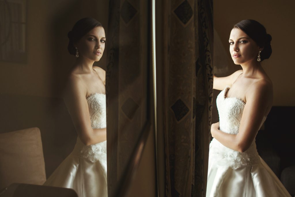 Happy bride looking at herself in the mirror wearing her dream wedding dress in an emotional moment